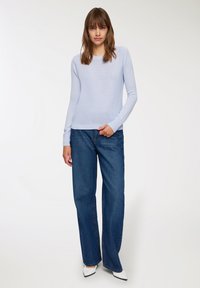 Jasnoniebieski sweter dzianinowy z długimi rękawami w połączeniu z luźnymi ciemnoniebieskimi dżinsami, białe buty na szpic, minimalistyczny design i ribbowe mankiety.