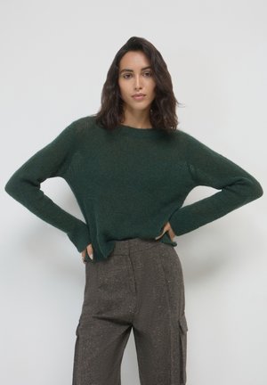 Maglione a maglia verde scuro con un fit rilassato, maniche lunghe e scollatura rotonda, abbinato a pantaloni marroni con texture.