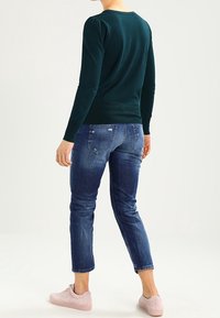 Tyrkysový svetr s dlouhým rukávem a nařasenými rameny, spárovaný s tmavě modrými slim džíny a světle růžovými teniskami. Jednoduchý ležérní design.