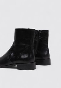 Botas de tobillo de cuero negro con textura suave, punta redonda, tacón bloque corto y cremallera lateral para ponerse fácilmente.