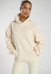 Felpa oversized color crema realizzata in morbido tessuto, con tasca a marsupio, cappuccio con cordino e polsini a coste.
