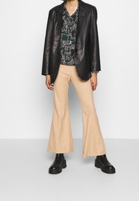 Zwarte leren blazer, groene en witte gestreepte shirt, beige flare broek en zwarte plateau laarzen. Soepele texturen en gestructureerde vormen.