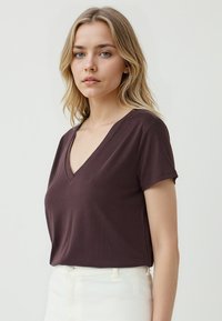 T-shirt marrone a maniche corte e scollo a V realizzato in un tessuto morbido, con una vestibilità rilassata e una texture liscia. Indossato con pantaloni bianchi a vita alta.