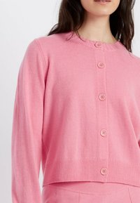 Cardigan rosa realizzato in morbido tessuto, con scollatura rotonda, orlo a costine e cinque bottoni abbinati sul davanti.