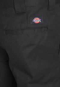 Poche arrière d'un pantalon Dickies noir avec un patch logo au-dessus de la poche sur un tissu durable, avec des passants de ceinture visibles.