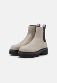 Botas chelsea de cuero gris claro con paneles laterales elásticos negros, punteras redondeadas y suelas negras gruesas con un patrón de banda.