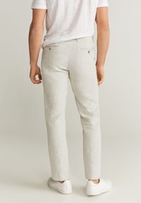 Lichtgrijze linnenbroek met een slim fit, voorzien van achterzakken met knopen en gecombineerd met witte sneakers. Gladde textuur, minimalistisch ontwerp.