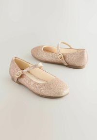 Bailarinas rosas con purpurina, con puntas redondeadas y suela plana, que cuentan con una correa al tobillo adornada con un acento dorado en forma de círculo. Forro interior suave.