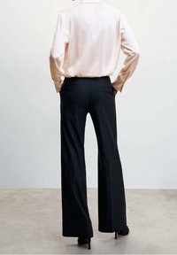 Blusa di satin rosa pallido con maniche lunghe, abbinata a pantaloni neri larghi a vita alta. Texture liscia e vestibilità su misura.