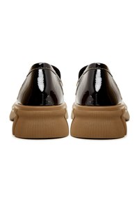 Paire de chaussures en cuir verni noir avec semelles épaisses en caoutchouc marron clair texturé, vue de dos sur fond blanc.