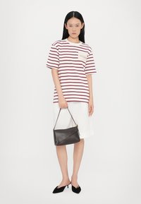 T-shirt rayé en blanc et bordeaux, associé à un short blanc. Sac à main en cuir noir au design élégant. Le mannequin porte des talons noirs.