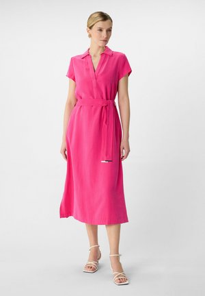 Roze, mouwloos jurkje met een V-hals en een strikceintuur. Glad materiaal, enkel-lang en lichtgewicht stof. Minimalistisch ontwerp.