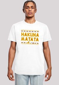 Hvit bomulls-kjorte med teksten "HAKUNA MATATA" i gul skrift, akkompagnert av tribal mønstre og dyregrafikk nederst.