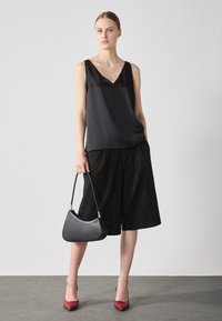 Black satin v-neck top, loose fit, paired with black wide-legged shorts. Accessory: curved black handbag with gold hardware, red high heels.
