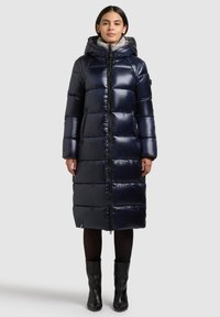 Tengerészkék steppelt pufi kabát kapucnival, cipzárral az elején és oldalzsebekkel. Elegáns, fényes anyagból; térdig érő, testhez simuló fazon.