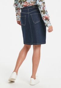 Mörk denimkjol i knälängd med två bakfickor, subtila sömnadsdetaljer och rak skärning. Bärs med en blommig långärmad topp och vita sneakers.