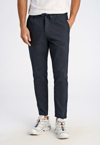 Marineblaue, leichte Hose mit verstellbarem Bund, schmalem Schnitt und zwei seitlichen Taschen, kombiniert mit weißen Sportschuhen.