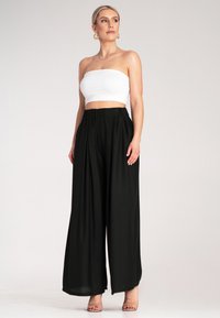 Czarne spodnie o szerokich nogawkach i luźnym kroju, z elastycznym paskiem w talii, zestawione z dopasowanym białym topem bez ramiączek. Gładki materiał o minimalnej teksturze.