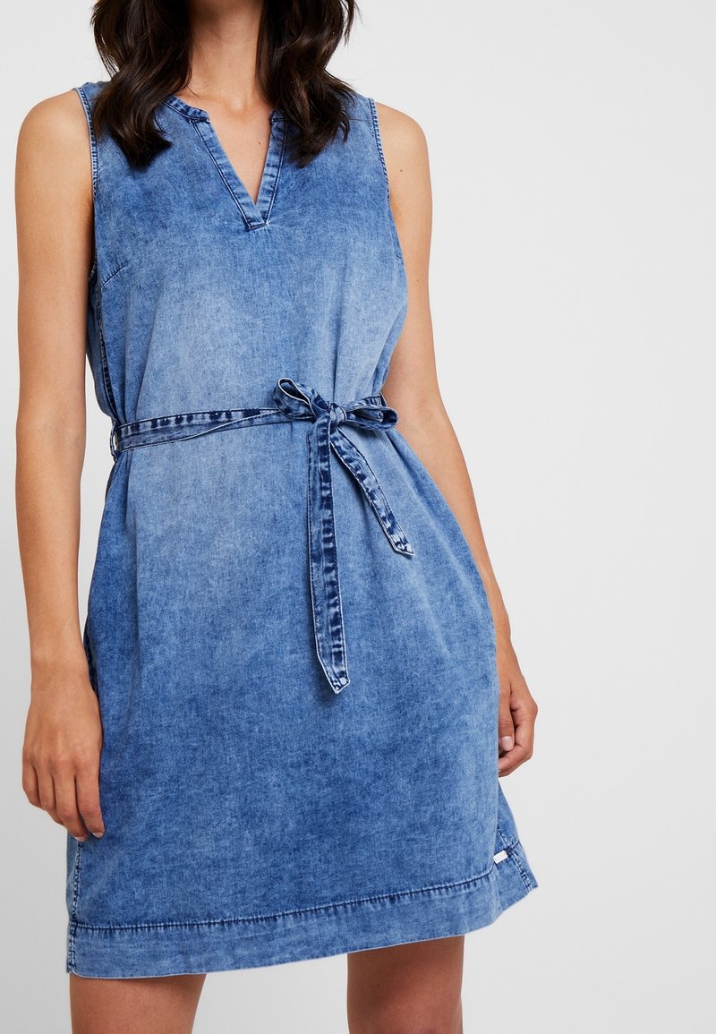 Džínové šaty s bezramenným designem, výstřihem do V, stahovacími pásky v pase a postupným přechodem od světle modré k tmavě modré. Mají rovný lem.