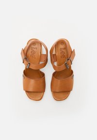 Sandálias de couro castanho com duas tiras largas cruzando o pé, tira no tornozelo ajustável com fivela de metal e solas planas. Logotipo da marca estampado por dentro.