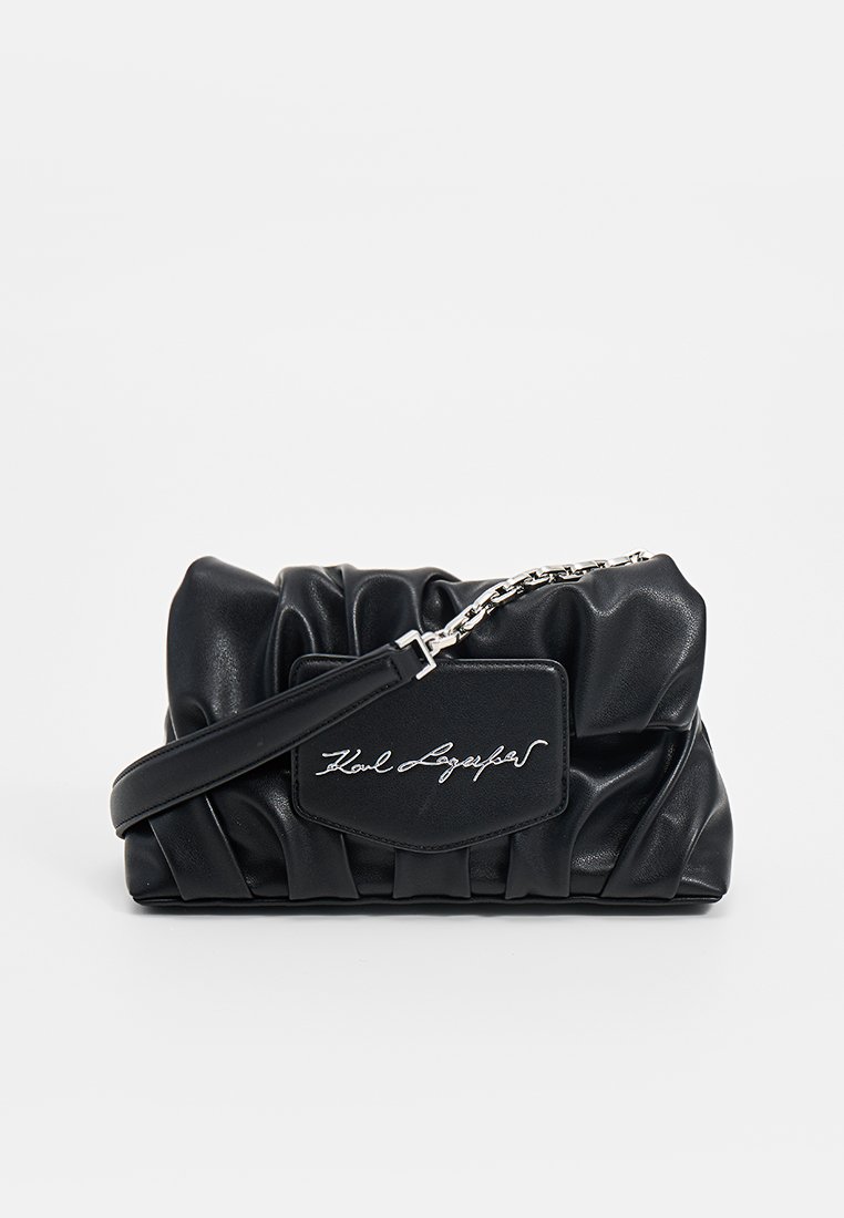 Bolso de mano de cuero negro con un diseño fruncido, que presenta una correa de cadena plateada y un parche de logo prominente en la parte frontal. Textura suave.