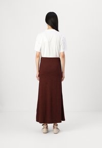 Hvit kortermet skjorte og lang, bordeaux skjørt. Skjørtet har en tettsittende midje og faller til anklene. Beige sko med ankelstropper.
