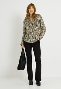 Blusa negra de manga larga con cuello puntiagudo, con un estampado de hojas en color crema; combinada con vaqueros negros acampanados y botas negras de tacón.