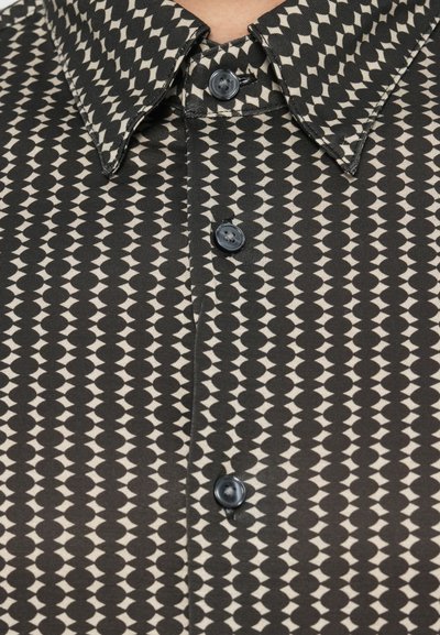 Marškiniai su sagomis, juodos ir kreminės spalvos geometriniu raštu, su apykakle ir juodomis sagomis, pagaminti iš tekstūruotos medžiagos.