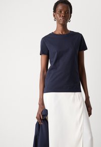 T-shirt in cotone blu navy con maniche corte e scollo rotondo, abbinato a una gonna bianca, il tessuto appare liscio e leggero.