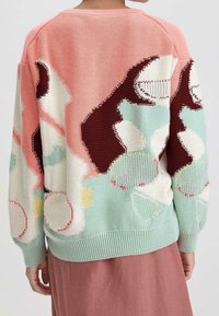 Pull en tricot avec une palette de couleurs pastel présentant des motifs floraux abstraits en rose, crème et vert menthe. Poignets et ourlet côtelés.