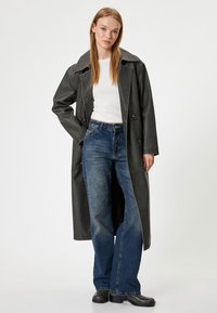 Manteau trench en simili cuir noir avec un large col ; associé à un jean en denim bleu à coupe ample et des bottines noires.