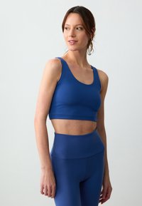 Top sportivo blu e leggings a vita alta abbinati, realizzati in un tessuto liscio ed elastico; design minimalista con scollo a barchetta e spalline larghe.