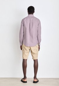 Camicia a quadri rossa e bianca, vestibilità rilassata con maniche lunghe, abbinata a pantaloni cargo beige. Sandali neri completano l'outfit.