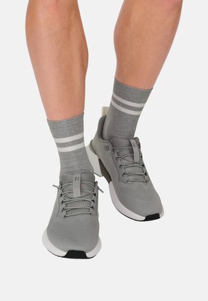 Graue Sportschuhe mit Mesh-Obermaterial und strukturierten Details, weißer Sohle und schwarzen Akzenten. Kombiniert mit grauen Socken mit weißen Streifen.