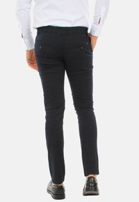 Pantaloni slim-fit blu navy in un tessuto liscio, con due tasche posteriori e un sottile dettaglio di branding. Indossati con scarpe nere, design minimalista.