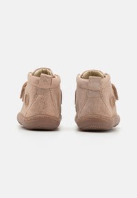 Zapatos de ante marrón con una textura suave, diseño de altura media y una correa de velcro a cada lado. Presentan un logo circular en el talón exterior.