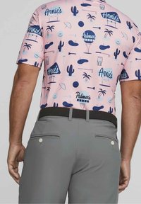 Polo rose à manches courtes présentant différents motifs bleus et bleu marine, incluant des cactus, des boissons et des logos. Associé à un pantalon gris et une ceinture noire.
