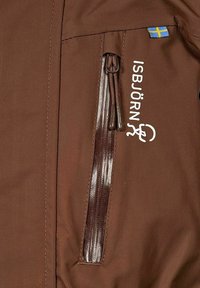 Brunt isolerad jacka i tyg med dragkedjeficka och logotyp i vitt. Inkluderar en liten blå och gul flaggdetalj. Slät textur.