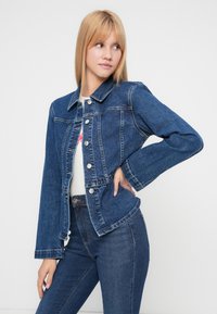 Τζιν μπουφάν σε σκούρο μπλε χρώμα με κλασικό γιακά, κουμπιά μπροστά και πλαϊνές τσέπες. Διαθέτει μακριά μανίκια με ελαφριά φουσκωτά στο τελείωμα.