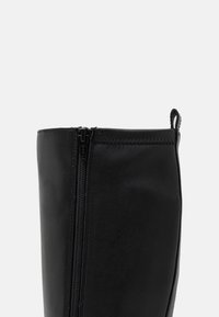 Stivale alla caviglia in pelle nera con zip laterale, texture liscia, punta arrotondata e una piccola linguetta sul retro.