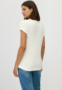 Witte, gestructureerde top met korte mouwen en een losse pasvorm, met een ronde halslijn en een licht gebogen zoom. Gekleed met lichtblauwe denim jeans.