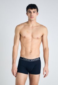 Sorte boxertruser laget av myk stoff med en kontrasterende hvit midjebånd med "TOMMY HILFIGER"-logo. Klassisk tett passform og glatt tekstur.