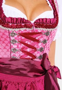 Vestido de dirndl rosa con un bodice ajustado adornado con patrones de corazones, acentos de satén, ribete de encaje y una falda acampanada con un lazo en la cintura.