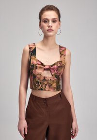 Crop top med levende blomsterprint i pink og grøn, med brede stropper og en sløjfedetalje foran. Brune højtaljede bukser.