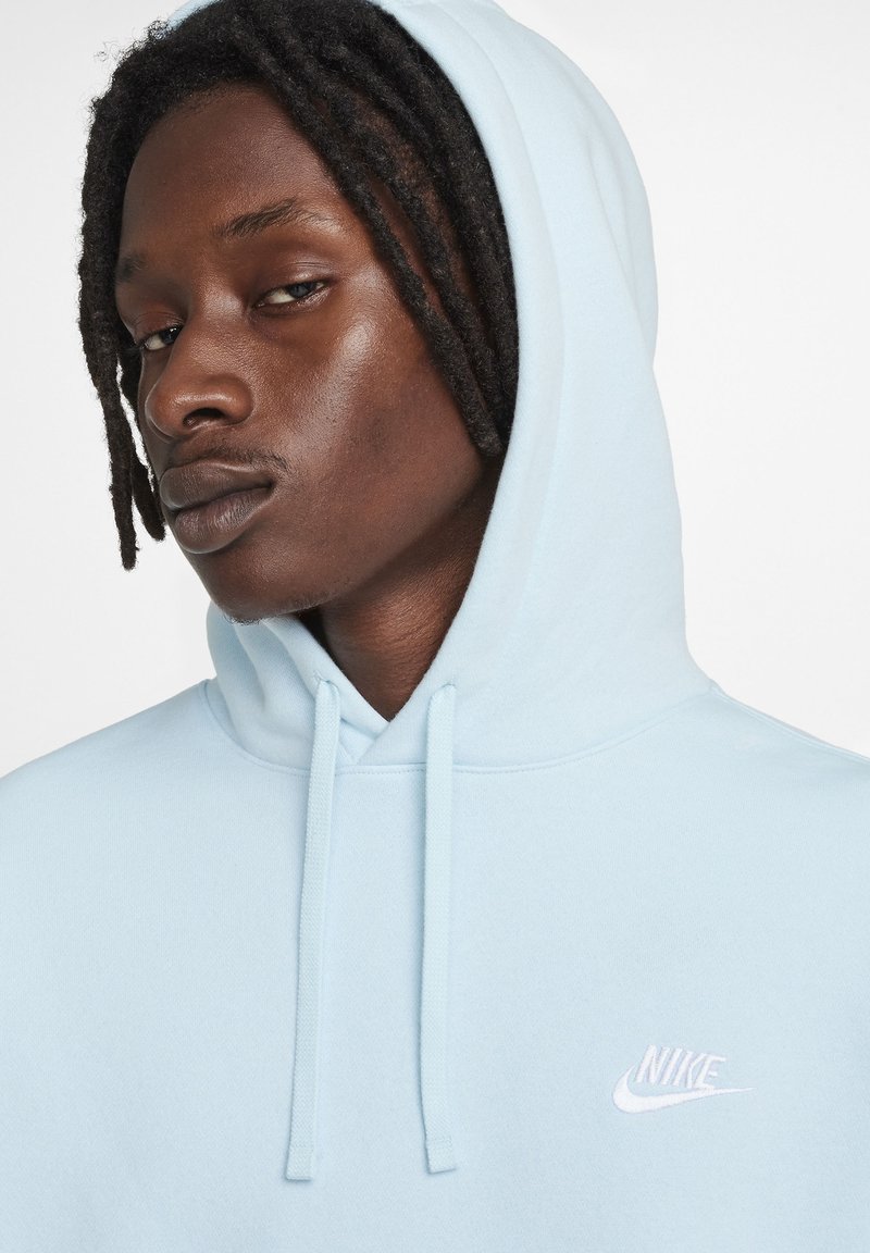 Sudadera azul clara con cordón, presenta un pequeño logo blanco de Nike en el pecho. Textura suave y corte relajado.