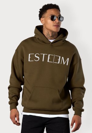 Olivgrüner Hoodie mit vorderer Tasche und weißem "ESTEEM"-Text, in lässiger Passform und mit gerippten Bündchen. Das Model trägt schwarze Sonnenbrillen.