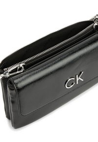 Černé psaníčko z lakované kůže s texturovaným povrchem, zipovým uzávěrem a stříbrným kováním. Na přední straně je logo a uvnitř je látková podšívka.