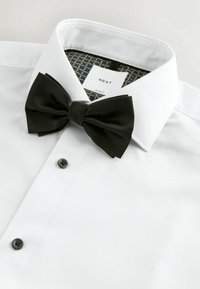 Weiße Slim-Fit-Hemd mit schwarzer Fliege, strukturiertem Stoff, Knopfdetails und gemusterter innerer Kragenfüllung mit Etikett.