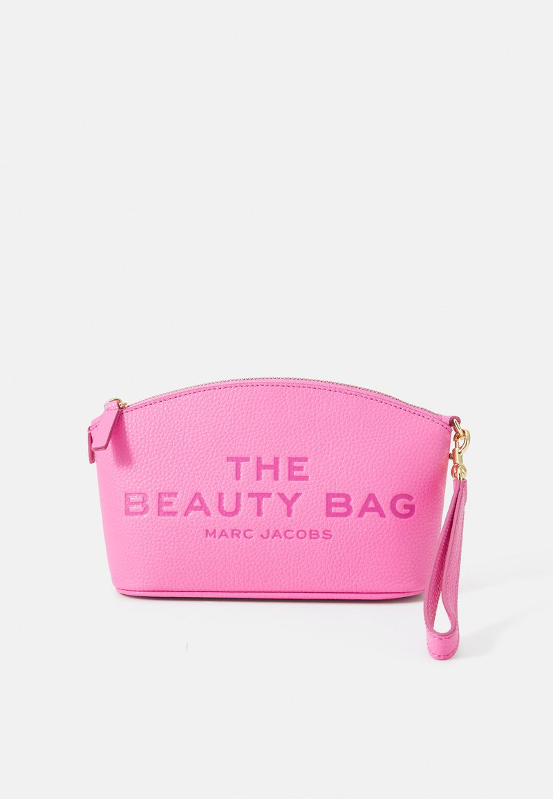 Roosa nahast kott kaarjalt ümarate servadega, millel on reljeefne tekst "THE BEAUTY BAG" ja "MARC JACOBS." Sisaldab randmepaela ja kuldset riistvara.