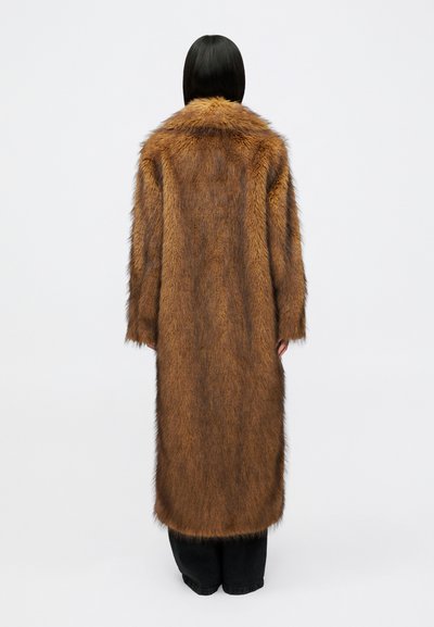 Hnedý kabát z umelého kožušina s širokým golierom, textúrovaným povrchom a dlhými rukávmi. Nosený cez čierne nohavice, vystavený na bielom pozadí.